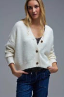 A woman wearing a cream-colored knit cardigan sweater with buttons, paired with dark blue jeans, shown against a plain light gray background.