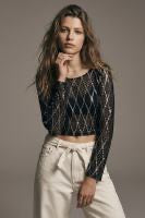A woman modeling a black long-sleeve crop top with a textured geometric pattern and white high-waisted pants against a plain gray studio background.